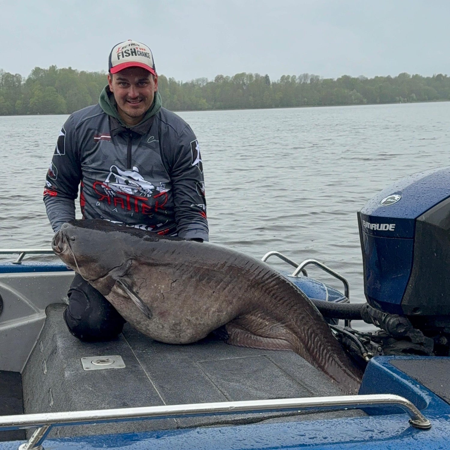 Person holding a large fish on a boat with a lake in the background